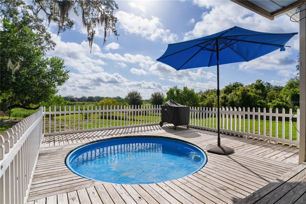 A round above-ground pool sits on a wooden deck with a blue umbrella and fence — 6590 CR 631, BUSHNELL, FL