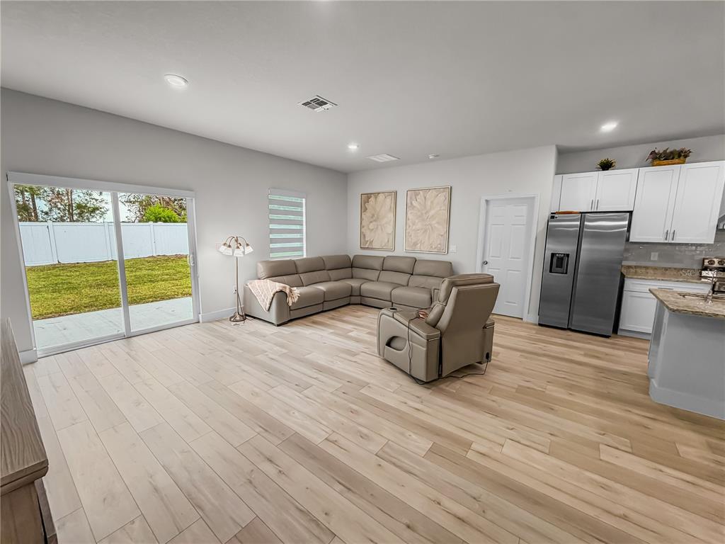 An open-concept kitchen and dining area features light wood flooring and blue upholstered chairs — 13340 SW 49TH AVENUE, OCALA, FL