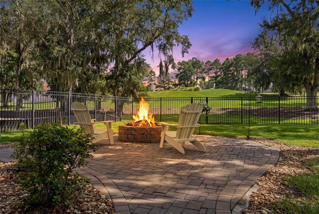 A brick patio with a fire pit and two chairs overlooks a fenced golf course — 4684 SOUTHERN VALLEY LOOP, BROOKSVILLE, FL