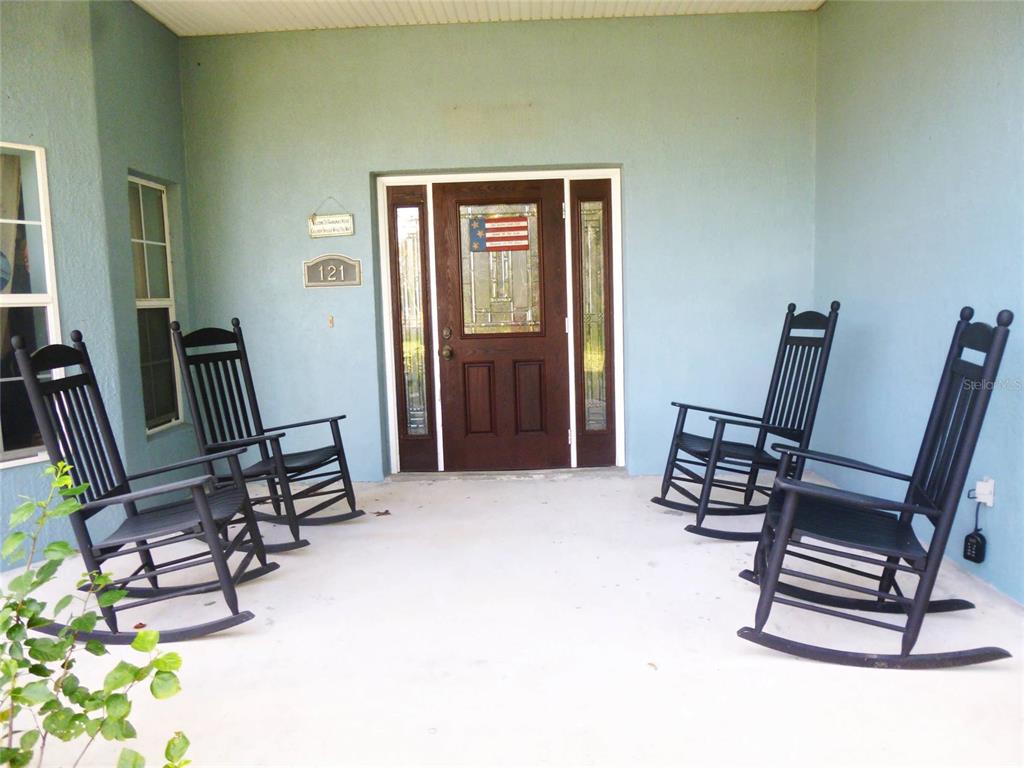 A covered front porch features light blue walls, a dark wood door, and four rocking chairs — 121 DEER ROAD, FROSTPROOF, FL