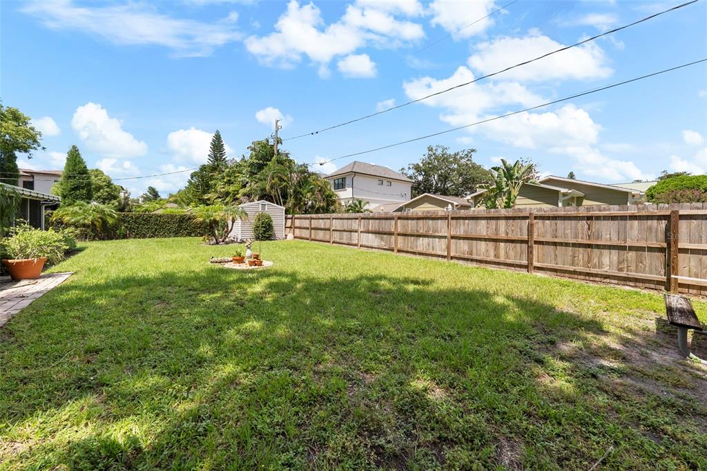 A grassy backyard features a wooden privacy fence, a small storage shed, and a bench — 3401 W SEVILLA STREET, TAMPA, FL