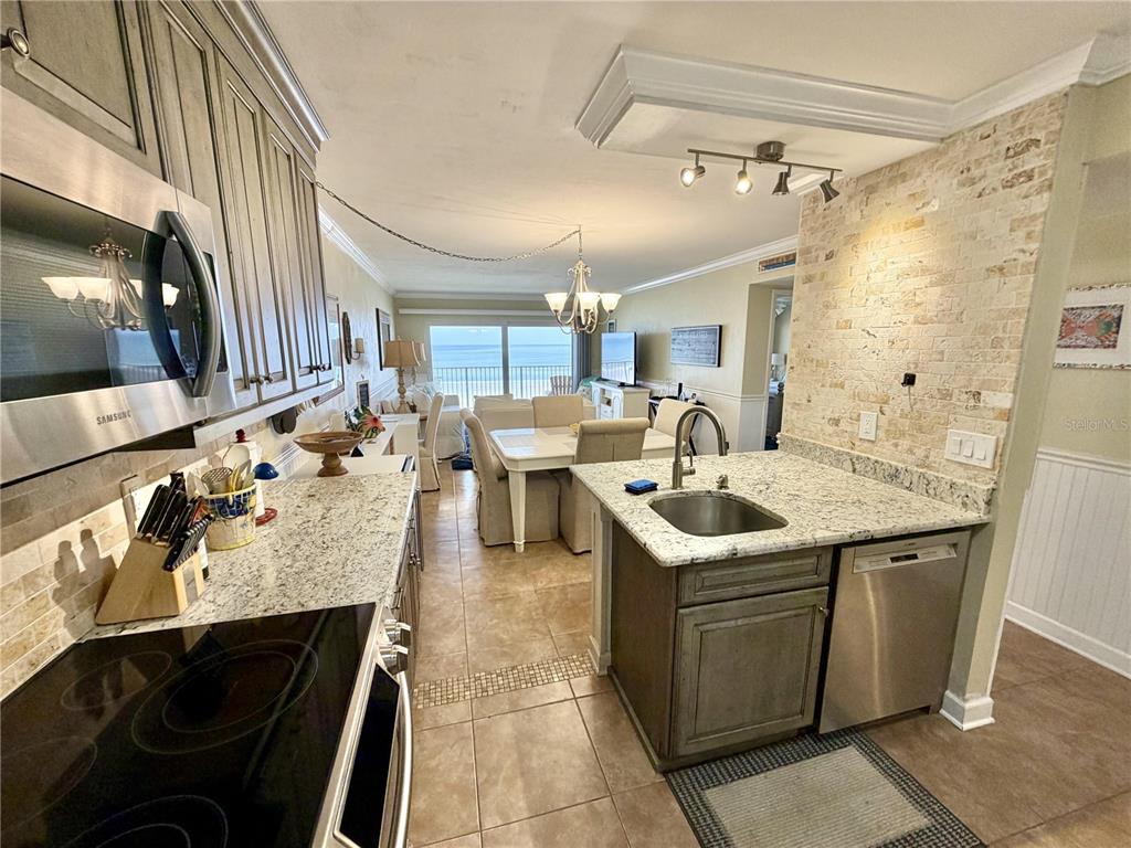 A kitchen with granite countertops and stainless steel appliances opens into a dining and living area — 4801 SAXON DR. UNIT A 202, NEW SMYRNA BEACH, FL