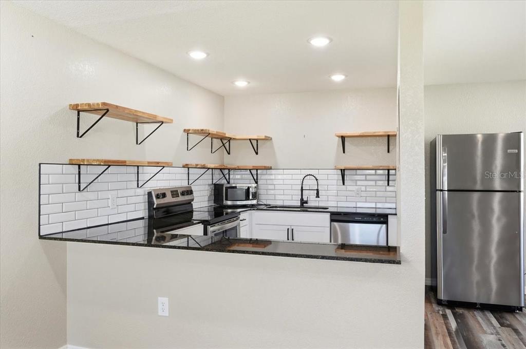 A kitchen features white cabinets, black countertops, subway tile backsplash, and open wood shelving — 205 ANDOVER PLACE N UNIT 119, SUN CITY CENTER, FL