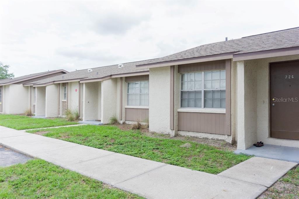 A row of single-story stucco apartment units features brown doors and a concrete sidewalk — 709 OCEANSIDE CIRCLE UNIT 712, RUSKIN, FL