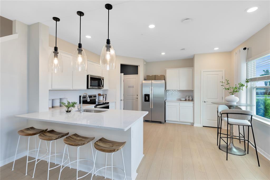A modern kitchen features white cabinetry, quartz countertops, a breakfast bar, and light wood flooring — 5114 MORNING DEW LANE, WEST MELBOURNE, FL