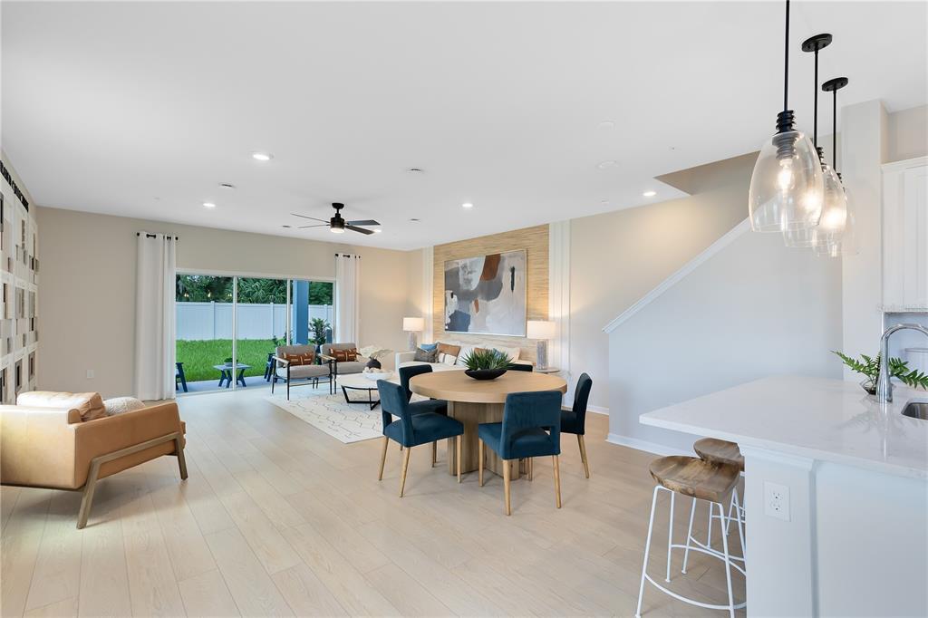 An open-concept living and dining area features light wood flooring, modern furniture, and sliding doors — 5114 MORNING DEW LANE, WEST MELBOURNE, FL