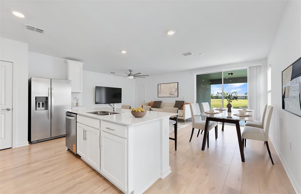 A modern open-concept kitchen and dining area with white cabinetry, stainless appliances, and wood flooring — 3033 WINDSWEPT WAY, WILDWOOD, FL