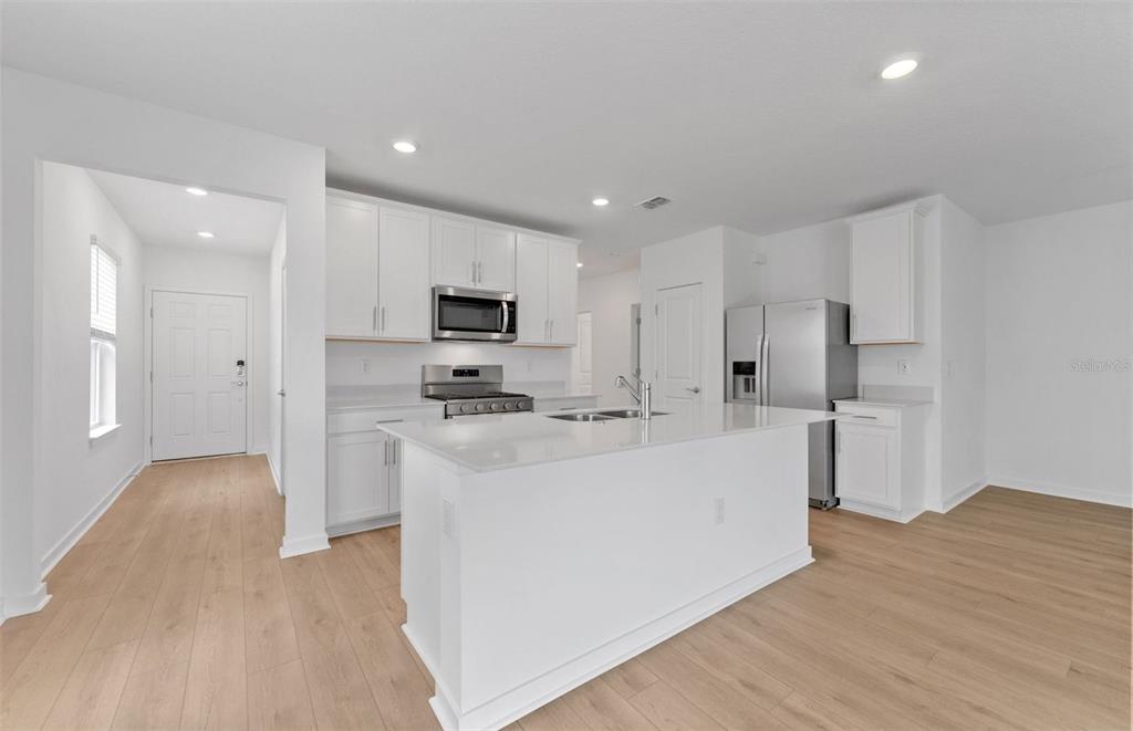 A modern kitchen features white cabinets, stainless steel appliances, and a central island with seating — 3033 WINDSWEPT WAY, WILDWOOD, FL