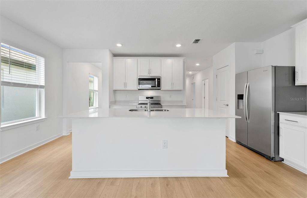 A modern kitchen features white cabinetry, a large central island, and stainless steel appliances — 3033 WINDSWEPT WAY, WILDWOOD, FL