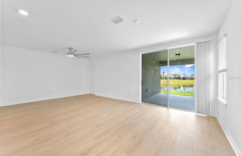 A bright living room with light wood-look flooring, a ceiling fan, and sliding glass doors — 3033 WINDSWEPT WAY, WILDWOOD, FL