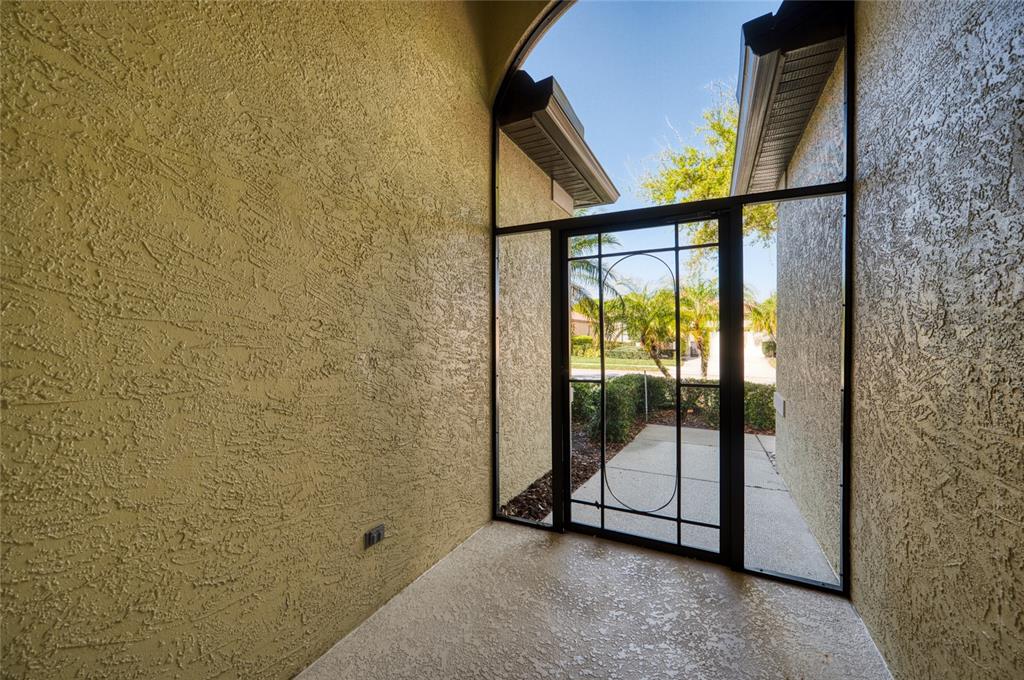 A covered entryway with textured yellow walls and a black metal screen door — 8142 STIRLING FALLS CIRCLE, SARASOTA, FL