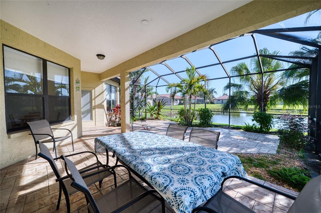 A covered patio features a dining set, tiled flooring, and a screened enclosure overlooking a pond — 8142 STIRLING FALLS CIRCLE, SARASOTA, FL
