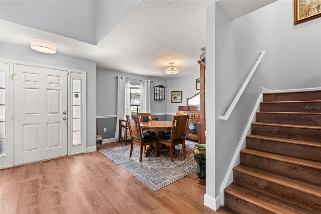 A dining area with a wooden table and chairs sits near an entryway and staircase — 302 LAKE SHEPARD DRIVE, APOPKA, FL