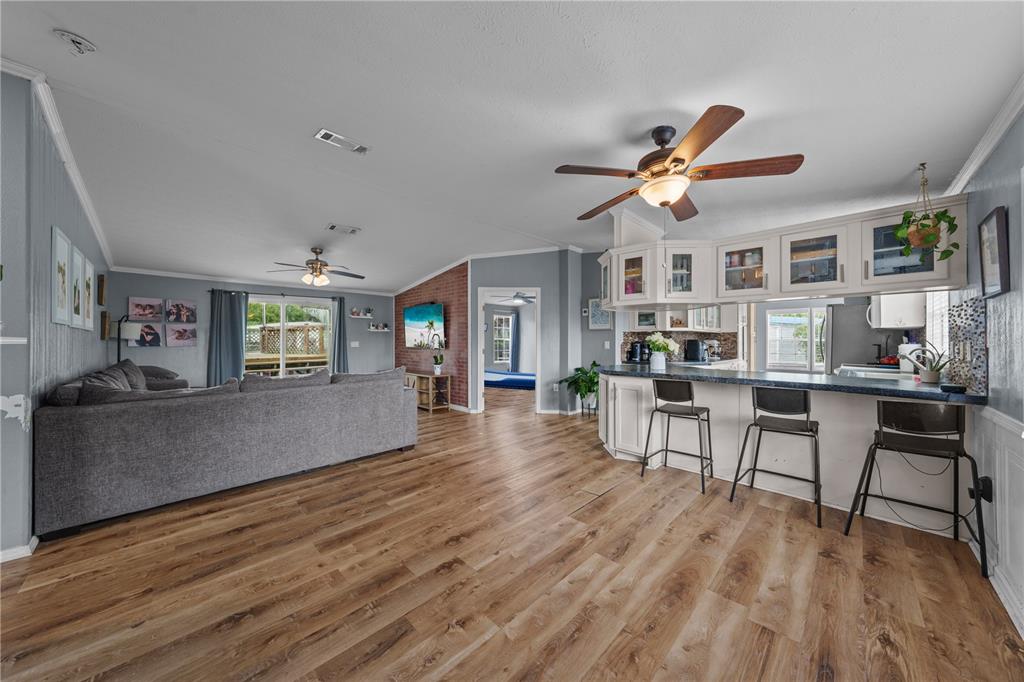 An open-concept living room and kitchen featuring wood-look flooring, a brick accent wall, and barstools — 6411 WOODS STREET, ST CLOUD, FL