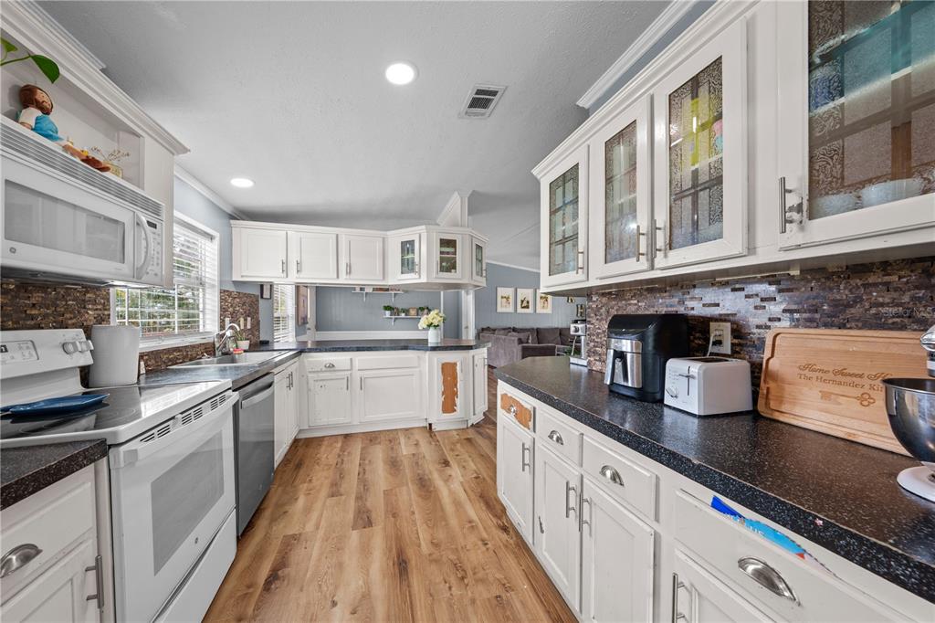 A kitchen features white cabinets, dark countertops, a tile backsplash, and light wood-look flooring — 6411 WOODS STREET, ST CLOUD, FL
