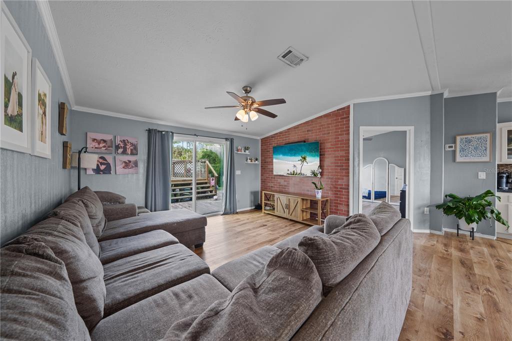 A living room features a brick accent wall, wood-look flooring, and a large sectional sofa — 6411 WOODS STREET, ST CLOUD, FL