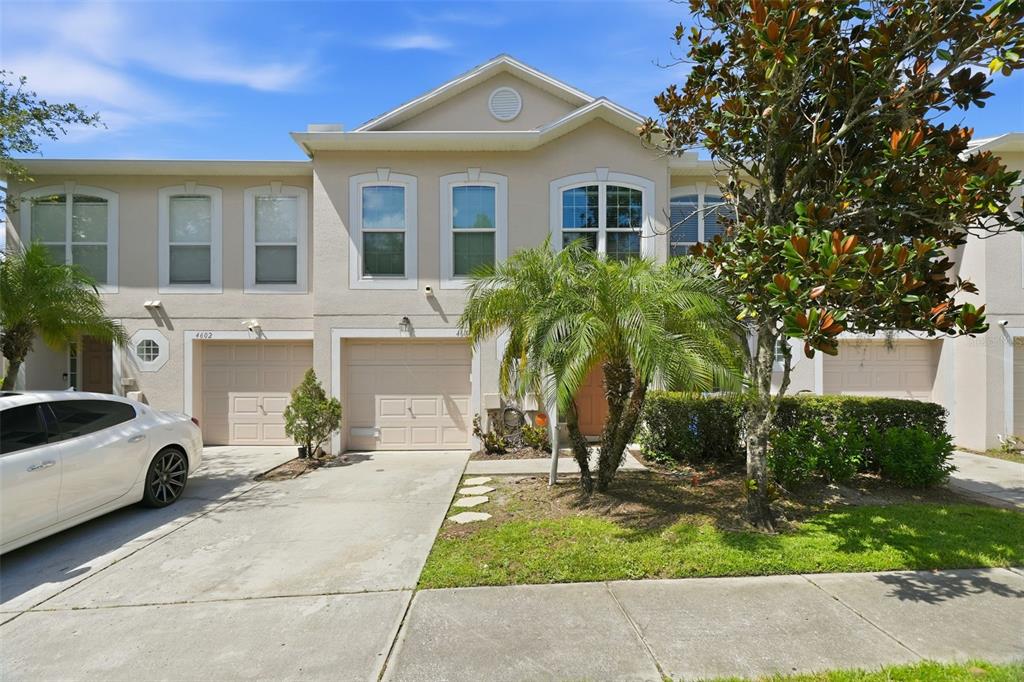 A two-story townhouse exterior with beige stucco, a palm tree, and two attached garages — 4604 ASHBURN SQUARE DRIVE, TAMPA, FL