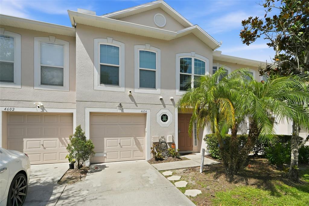 A two-story townhouse exterior features beige stucco, a garage, and a small front palm tree — 4604 ASHBURN SQUARE DRIVE, TAMPA, FL