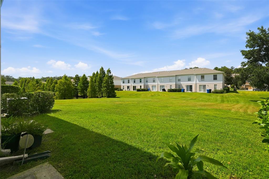 A grassy backyard area extends toward a multi-unit residential building under a blue sky — 4604 ASHBURN SQUARE DRIVE, TAMPA, FL