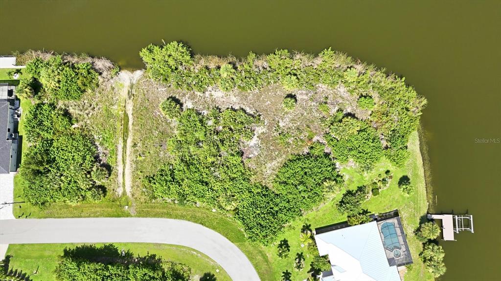 An aerial view shows a vacant, wooded waterfront lot next to a residential house — 15296 ALDAMA CIRCLE, PORT CHARLOTTE, FL