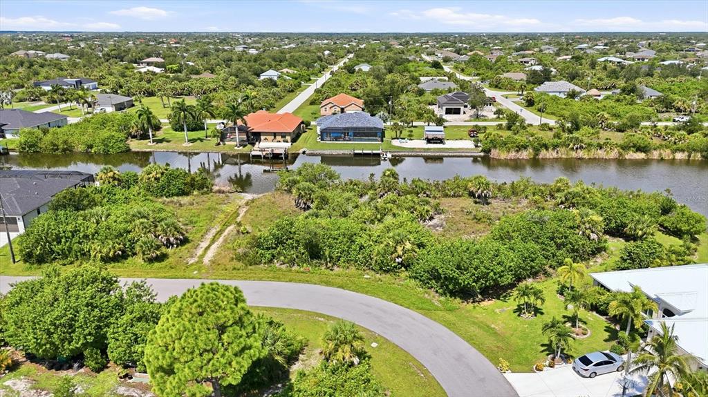 An aerial view shows a vacant lot with vegetation bordering a canal near residential houses — 15296 ALDAMA CIRCLE, PORT CHARLOTTE, FL