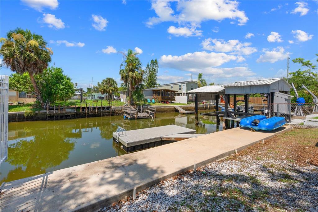 A concrete dock and boat lift sit along a canal with palm trees and houses — 6833 FLICKER LANE, HUDSON, FL