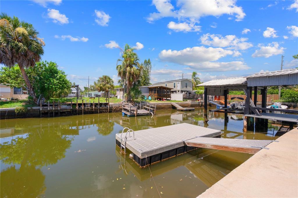 A floating dock sits in a canal in front of a house with a boat lift — 6833 FLICKER LANE, HUDSON, FL