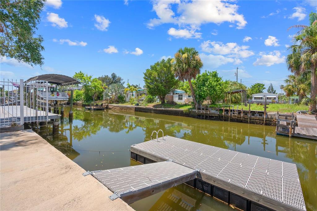 A floating dock sits in a canal next to a boat lift and grassy yard — 6833 FLICKER LANE, HUDSON, FL