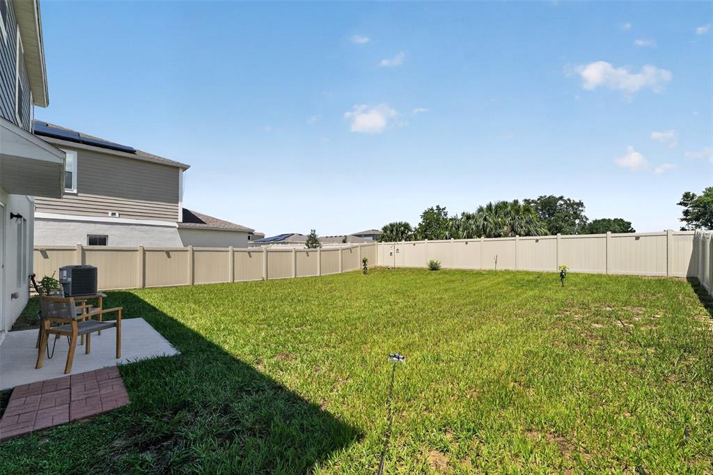 A fenced backyard features a small concrete patio with outdoor furniture and a grassy lawn — 1857 GRASMERE STREET, HAINES CITY, FL