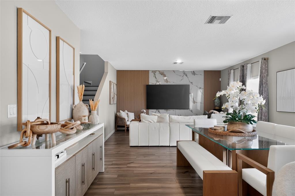 A modern living and dining area features wood-slat walls, a marble accent wall, and wood flooring — 1857 GRASMERE STREET, HAINES CITY, FL