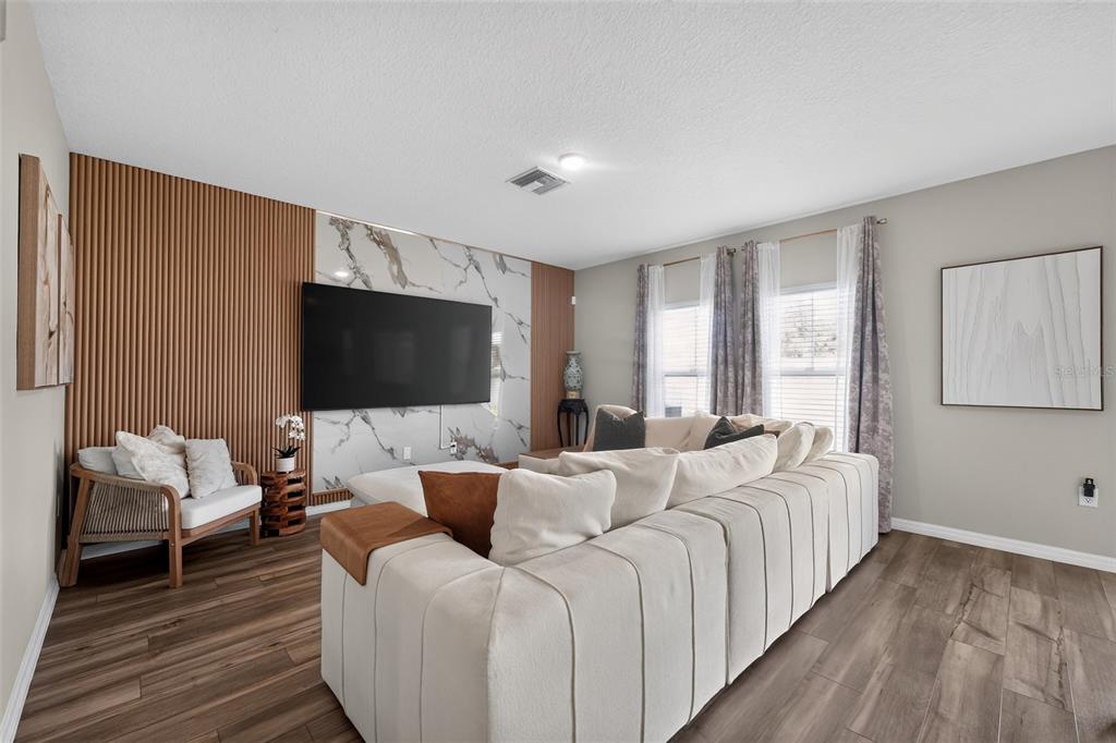 A living room features a large sectional sofa, a marble-accented television wall, and wood-slat paneling — 1857 GRASMERE STREET, HAINES CITY, FL