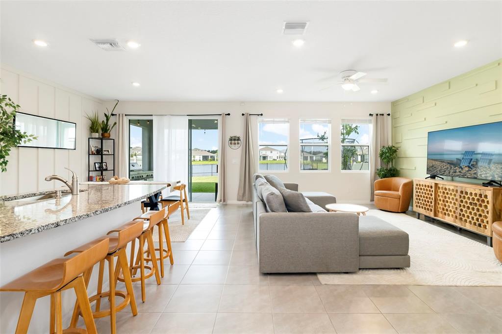 This open-concept living area features a kitchen island, gray sectional sofa, and a television wall — 523 158TH STREET E, BRADENTON, FL