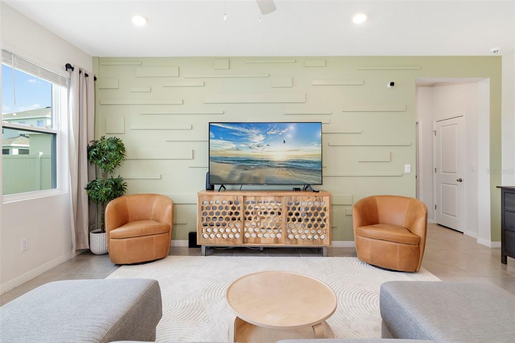 A living room features a sage green accent wall with horizontal trim, two leather chairs, and a television — 523 158TH STREET E, BRADENTON, FL