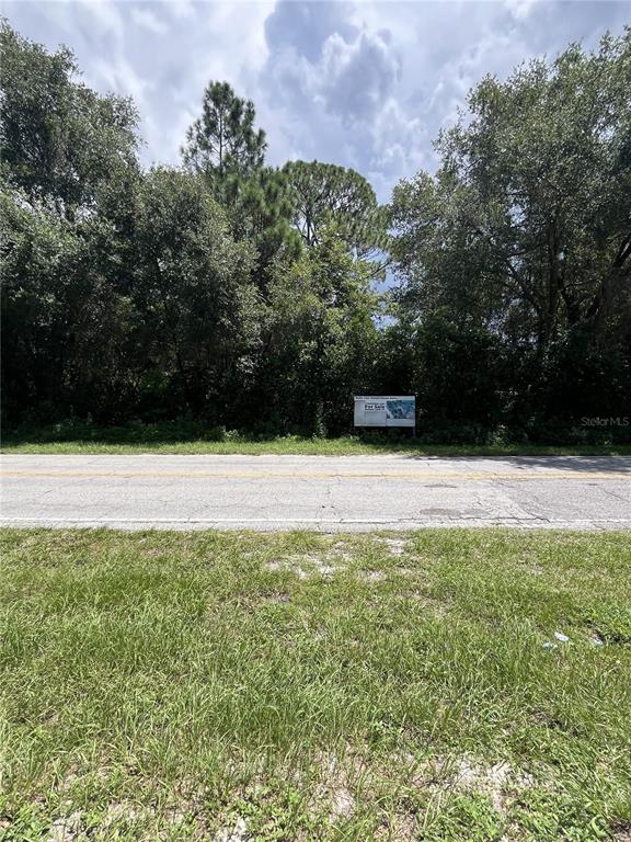 A vacant, wooded lot with a for sale sign sits behind a paved road — 847 LARK COURT, DELTONA, FL