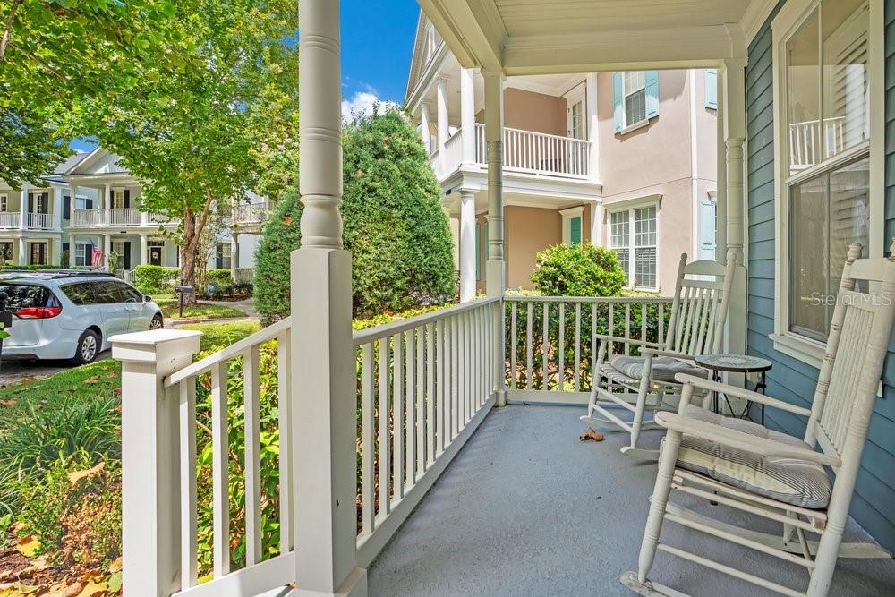 A covered front porch features white railings, two rocking chairs, and a view of neighborhood homes — 1205 GREENE SQUARE, CELEBRATION, FL
