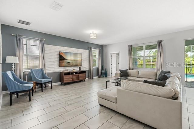 A living room features a textured accent wall, a television, and light-colored tile flooring — 8909 STINGER DRIVE, CHAMPIONS GATE, FL