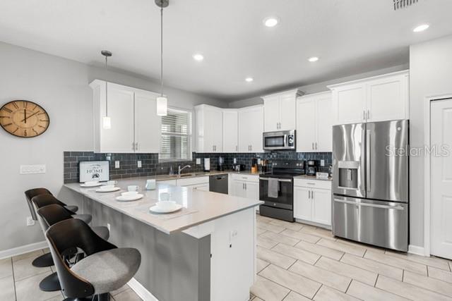 A modern kitchen features white cabinetry, stainless steel appliances, and a breakfast bar with stools — 8909 STINGER DRIVE, CHAMPIONS GATE, FL