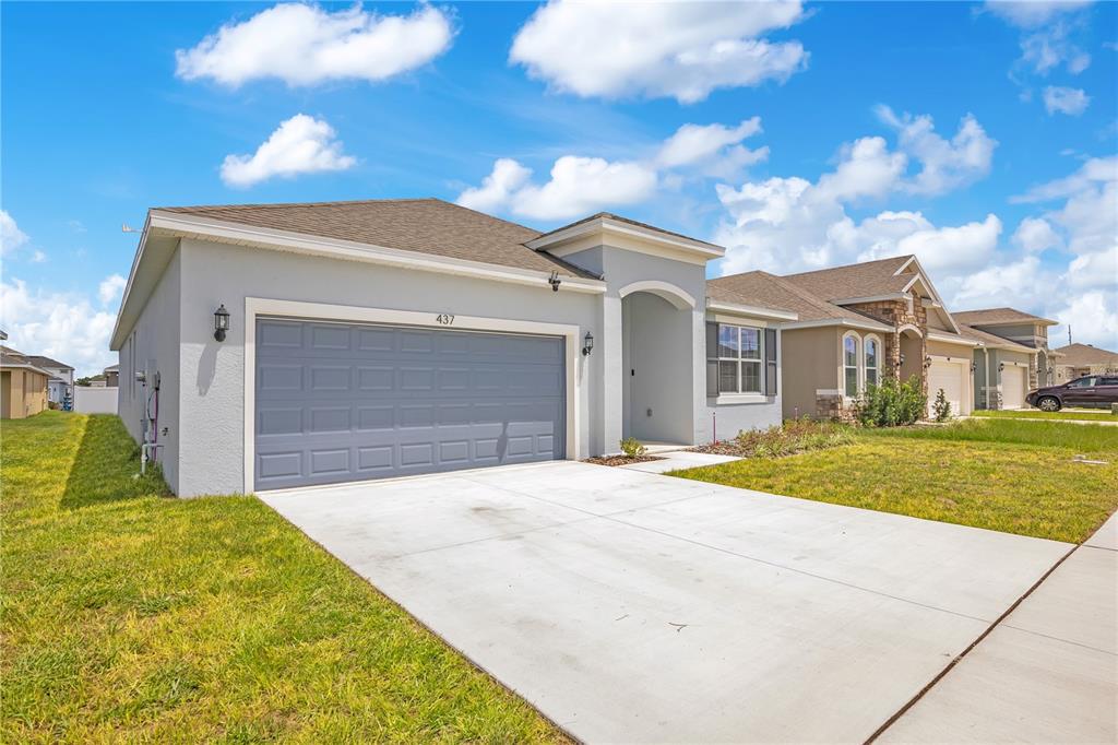 A single-story house with a gray garage door, light-colored stucco exterior, and a concrete driveway — 437 SILVER PALM DRIVE, HAINES CITY, FL