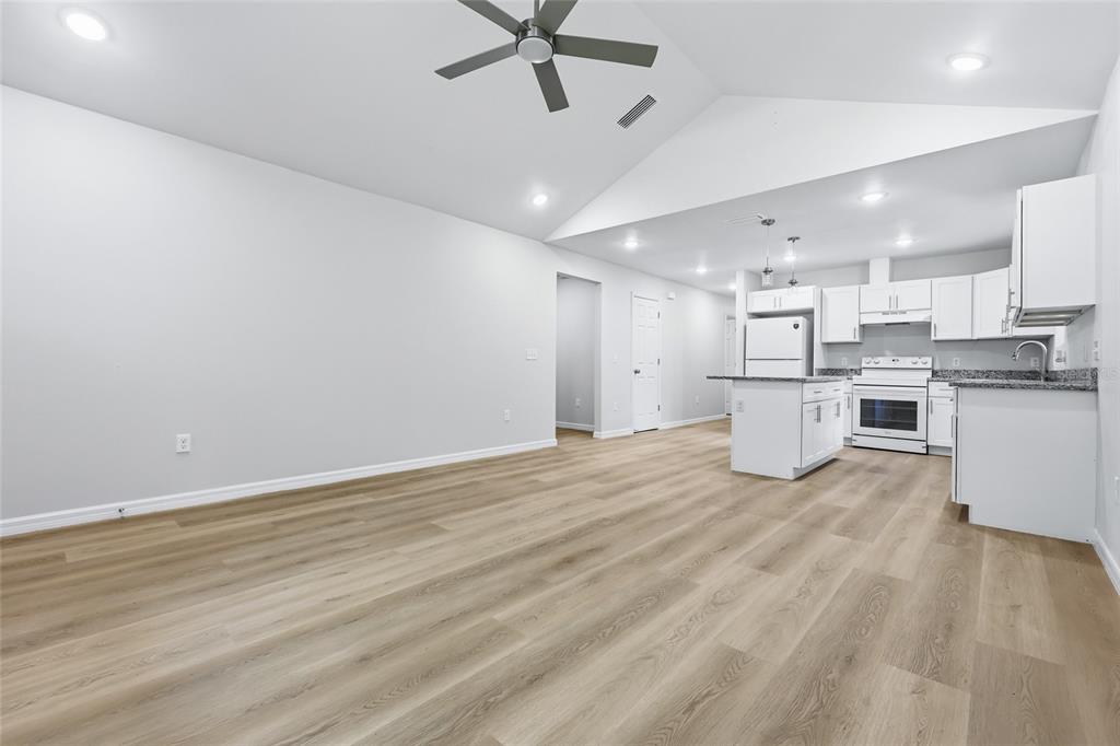 An empty room with light wood-look flooring, a vaulted ceiling, a ceiling fan, and a door — 2447 SE 10TH AVENUE, GAINESVILLE, FL