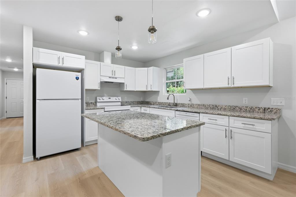 A kitchen features white cabinets, granite countertops, a kitchen island, and white appliances — 2447 SE 10TH AVENUE, GAINESVILLE, FL