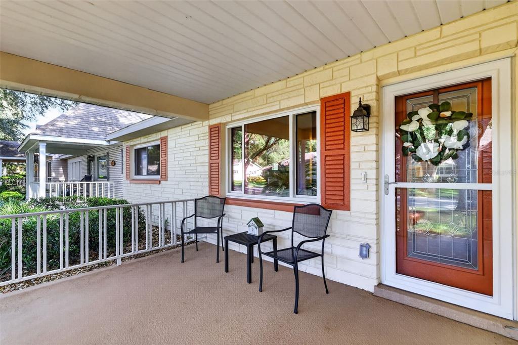 A covered front porch features a white railing, two metal chairs, and a glass storm door — 8591 SW 93RD PLACE UNIT C, OCALA, FL