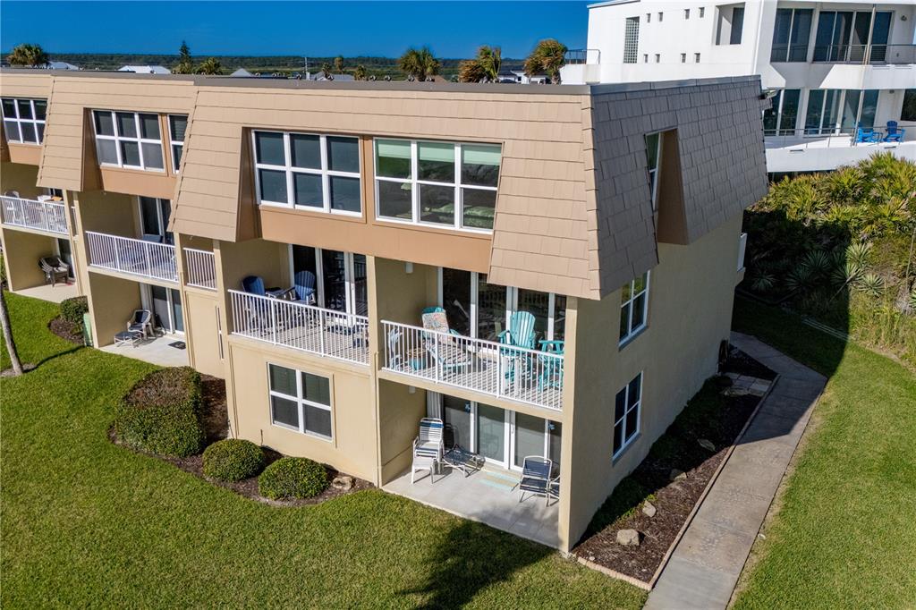 An elevated exterior view of a multi-story tan apartment building with balconies and a lawn — 7900 A1A S UNIT A214, ST AUGUSTINE, FL