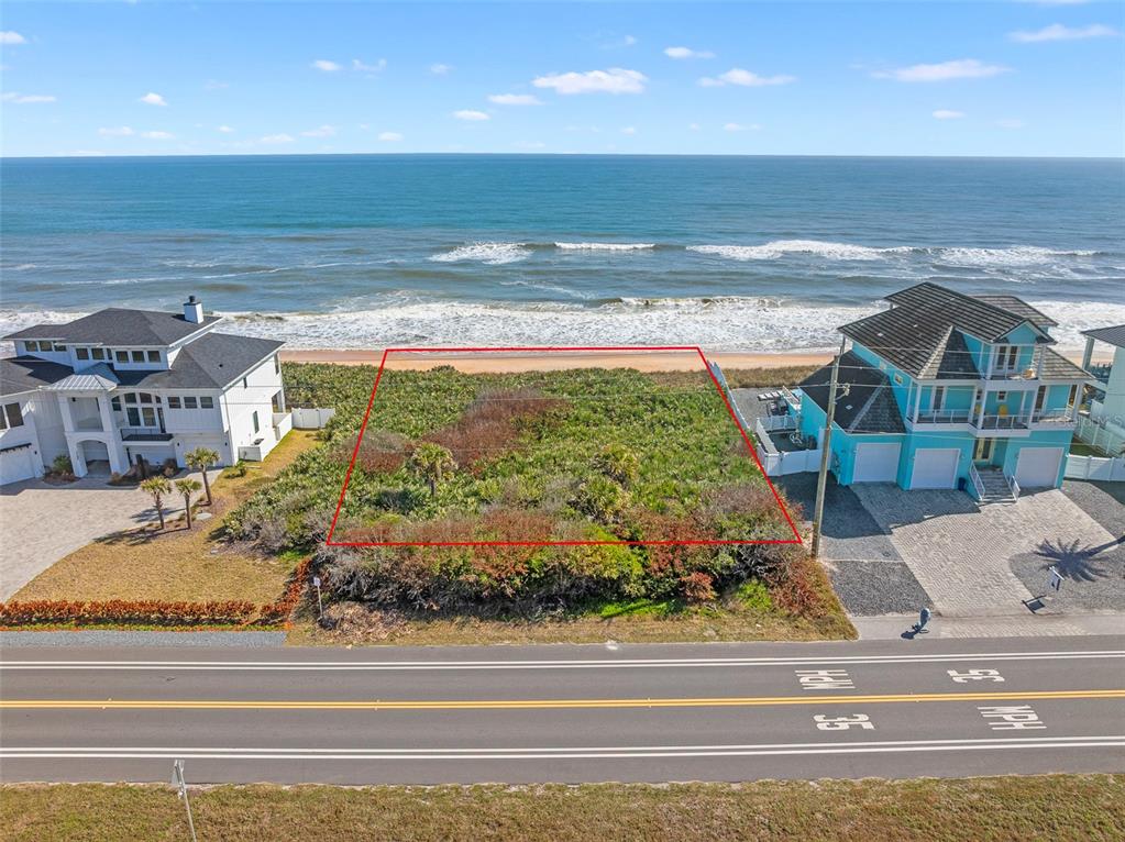 An aerial view shows a vacant, brush-covered oceanfront lot situated between two large houses — 3101 N OCEAN SHORE BOULEVARD, FLAGLER BEACH, FL