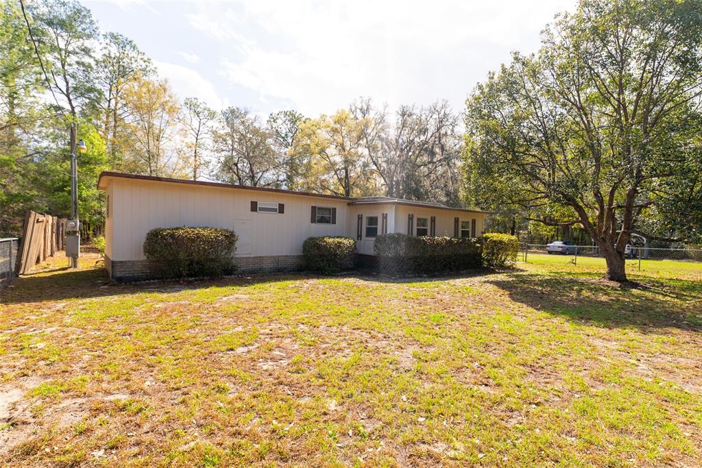 A white storage shed with brown trim and double doors sits in a wooded yard — 14881 NE 147TH AVENUE, FORT MC COY, FL