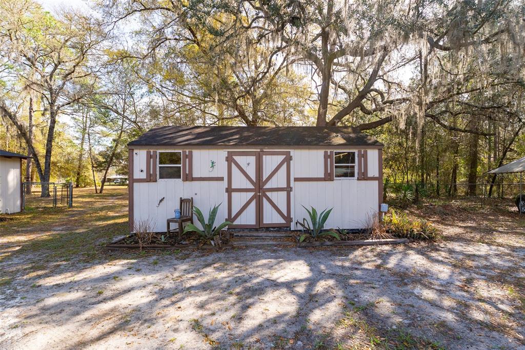 A small, light-colored shed with a single door and a window sits in a yard — 14881 NE 147TH AVENUE, FORT MC COY, FL