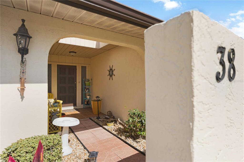 A paved walkway leads to the covered entrance of a home with a numbered pillar — 38 PEBBLE ROCK DRIVE, VENICE, FL