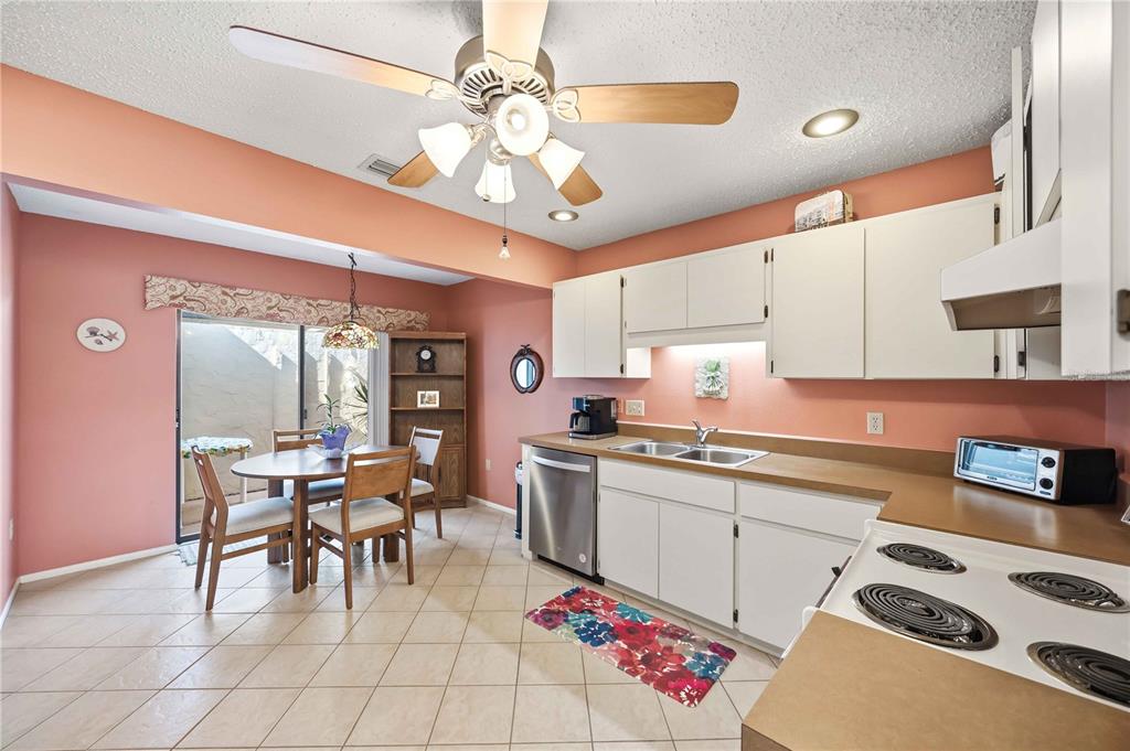 A kitchen with peach walls, white cabinets, tan countertops, and an adjacent dining area — 38 PEBBLE ROCK DRIVE, VENICE, FL