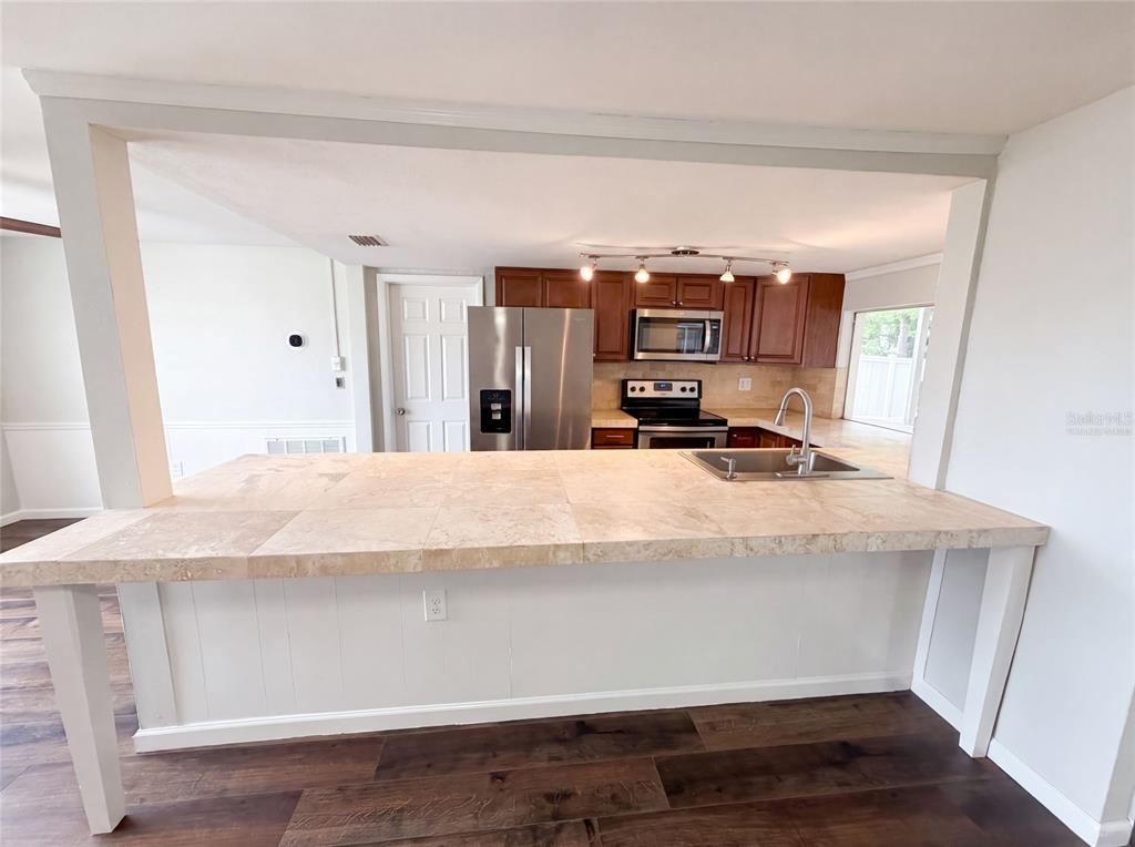 A kitchen features a large tiled breakfast bar, stainless steel appliances, and dark wood cabinetry — 3400 BAINBRIDGE DRIVE, HOLIDAY, FL