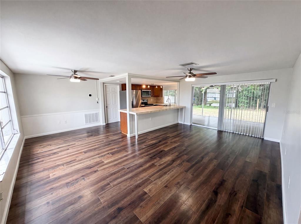 An open-concept living area features wood-look flooring, a kitchen island, and sliding glass patio doors — 3400 BAINBRIDGE DRIVE, HOLIDAY, FL