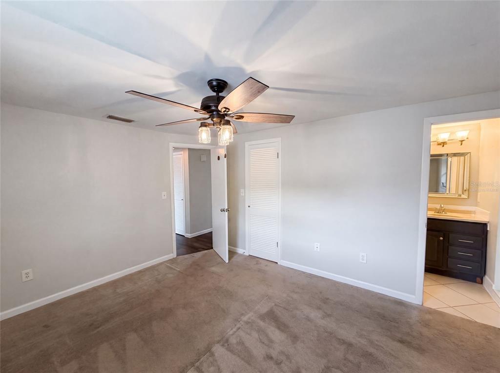 A carpeted bedroom features a ceiling fan, a closet with louvered doors, and an attached bathroom — 3400 BAINBRIDGE DRIVE, HOLIDAY, FL